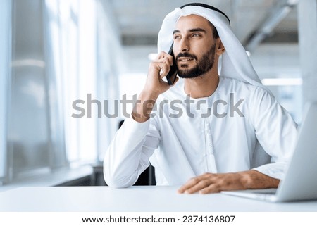 handsome man with dish dasha working in his business office of Dubai. Portraits of a successful businessman in traditional emirates white dress. Concept about middle eastern cultures. Royalty-Free Stock Photo #2374136807