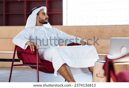 handsome man with dish dasha working in his business office of Dubai. Portraits of a successful businessman in traditional emirates white dress. Concept about middle eastern cultures. Royalty-Free Stock Photo #2374136813