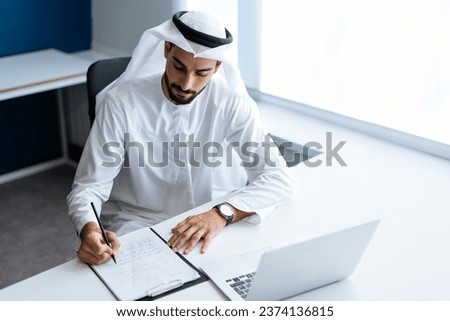 handsome man with dish dasha working in his business office of Dubai. Portraits of a successful businessman in traditional emirates white dress. Concept about middle eastern cultures. Royalty-Free Stock Photo #2374136815