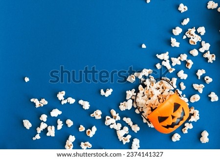 Jack o lantern basket full of popcorn on a blue background with copy space. Halloween banner. Autumn or fall movie concept.  Movie night concept. Watching TV themed photo. 