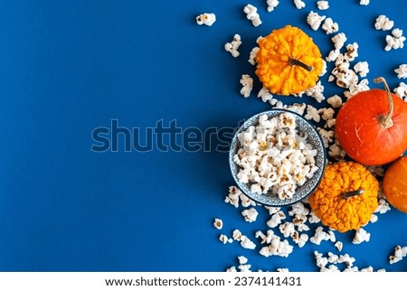 Popcorn and decorative pumpkins with TV remote on a blue background with copy space. Movie night concept. Wateching TV themed photo. Fall or autumn TV shows.