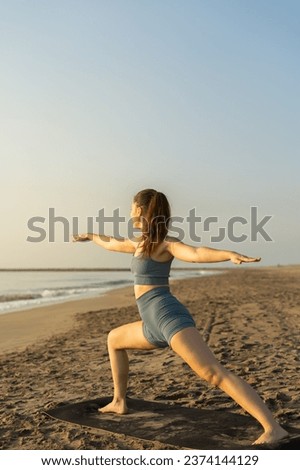 athletic young lady practicing yoga in sports wear in front of the beach. yoga warrior pose. pilates concept
