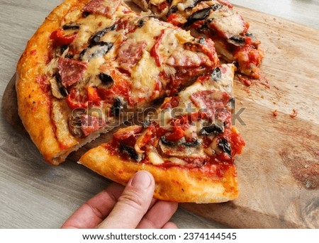 A man's hand takes a cut slice of pizza from a wooden board. High quality photo