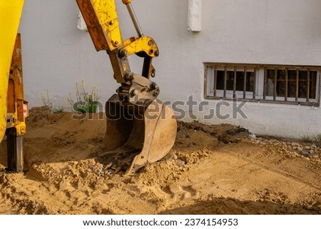 Fragment of a yellow excavator with a bucket lowered onto the sand at a construction site Royalty-Free Stock Photo #2374154953