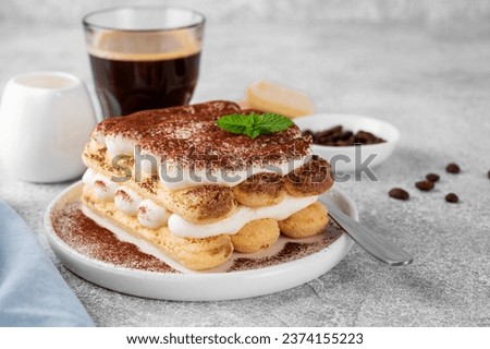 Tradition italian layered dessert tiramisu with mascarpone cream and biscuits on a white plate with cup of coffee on a gray concrete background Royalty-Free Stock Photo #2374155223