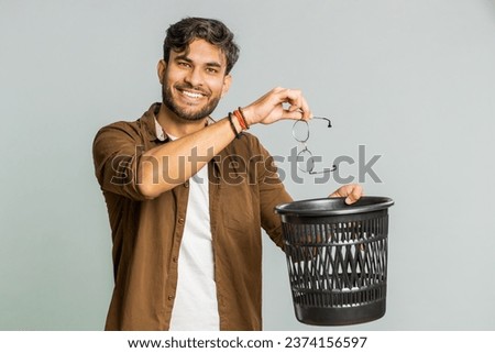 Indian young man taking off throwing out glasses into bin after medical vision laser treatment therapy surgery looking smiling at camera, heal, cure. Arabian guy isolated on studio gray background Royalty-Free Stock Photo #2374156597