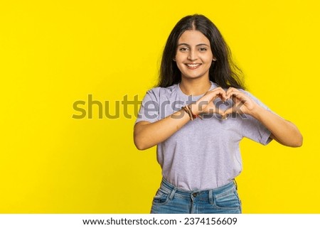 Woman in love. Smiling attractive Indian woman makes heart gesture demonstrates love sign expresses good positive feelings and sympathy. Arabian Hindu young girl isolated on yellow wall background Royalty-Free Stock Photo #2374156609