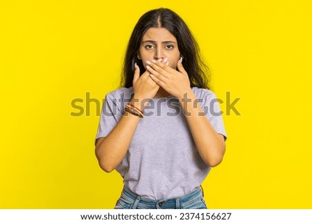 I will not say anything. Frightened Indian woman closing mouth with hands, looking intimidated scared at camera gestures no, refusing tell terrible secret unbelievable truth. Girl on yellow background Royalty-Free Stock Photo #2374156627