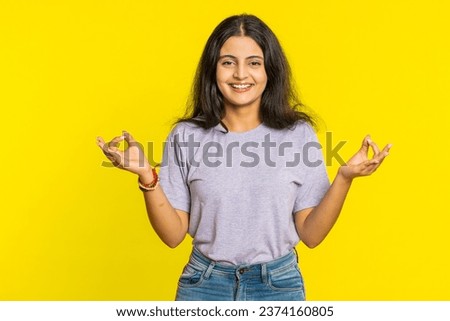 Keep calm down, relax, rest. Concentrated happy Indian woman meditating breathes deeply with mudra yoga gesture, eyes closed, peaceful mind, taking a break. Arabian Hindu girl on yellow background