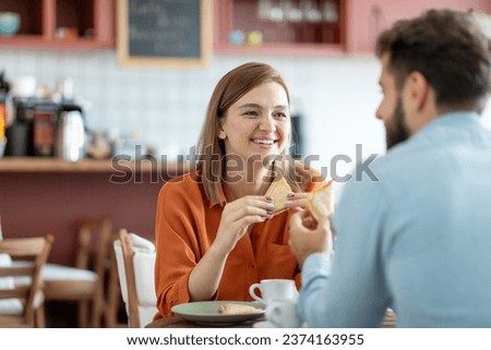 Young cheerful caucasian couple drinking coffee and eating sandwiches in coffee house or cafe, enjoying pleasant talk indoors. People, date, love and lifestyle concept Royalty-Free Stock Photo #2374163955