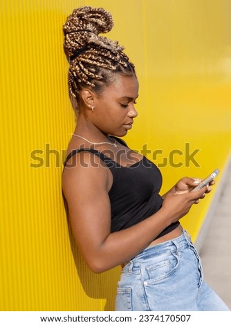 Portrait of young beautiful  woman with a long braids holding phone in her hands on a yellow