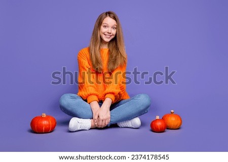 Full length photo of cute teenager girl sitting floor crossed legs comfortable halloween atmosphere isolated on violet color background