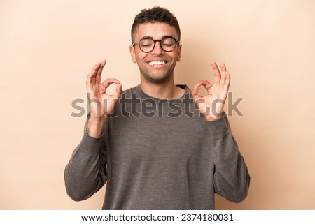 Young Brazilian man isolated on beige background in zen pose