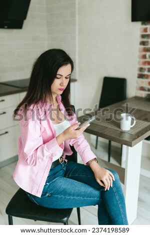 A young girl with black hair in a pink shirt sits at a table with a phone and a white mug in a cozy room with brown brick. Woman working, talking on the phone, drinking coffee in a modern cafe.Morning