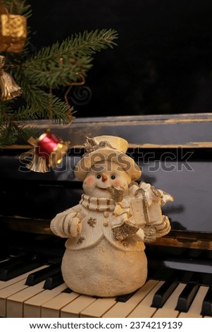Decorative figurine of a snowman with a Christmas tree on a old shabby piano. Festive new year decor, warm dark composition
