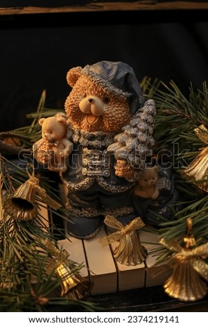 Decorative figurine of a bear with a Christmas tree on a piano, decorated with a pine tree and bells. Festive new year decor, warm dark composition