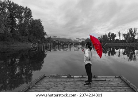 A concept digitally enhanced photo of a black and white photo of a woman standing on a dock holding a red umbrella by the Kootenai River in North Idaho.