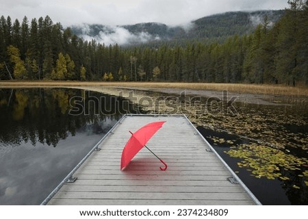 A concept photo of a red umbrella resting on a small dock at Sinclair Lake in the far north part of Idaho during autumn.