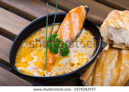 Picture of delicious cream-soup with salmon and greens, served in bowl with bread at table
