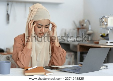 Young Asian Muslim businesswoman sitting for long hours working with laptop computer at home office. Have symptoms of fatigue, headaches, and stress from work. office syndrome symptoms