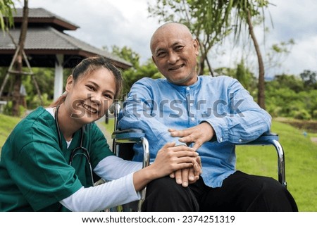 Friendly young Asian nurse with old man on wheelchair in park