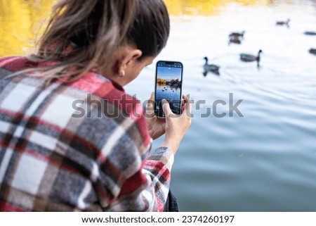 A woman takes a photo on her smartphone. Photo of a city pond with ducks on a smartphone.