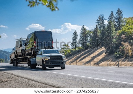 Gray industrial carrier car hauler heavy duty truck transporting mini vans on the long semi trailer driving on the one way highway road intersection in California mountains Royalty-Free Stock Photo #2374265829