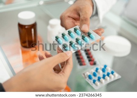 Pharmacist recommends medicines to customers. Asking the questions of medication. Professional Asian male pharmacist giving prescription medications to female patient customers at drugstore shelves. Royalty-Free Stock Photo #2374266345
