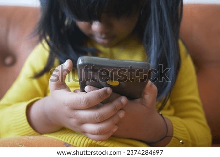 Child girl in yellow dress watching cartoon on smart phone 