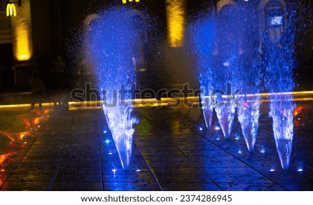 Blue fountain, streams and splashes of water at night. Light fountain. Bright colored lanterns illuminate the water at night. Beautiful dark background.