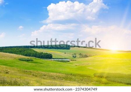 Green meadow (grassland) on a hilly landscape and Sky with bright sunise.