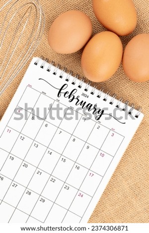 February 2024 Desk calendar and fresh eggs with egg whisk on burlap background.