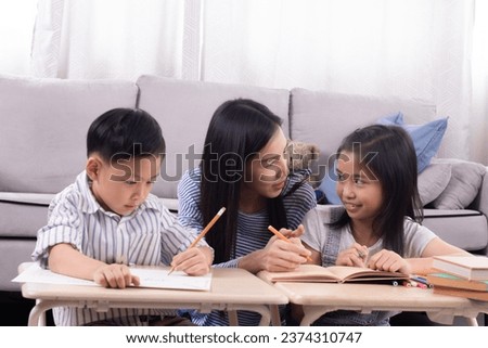 Cheerful Asian mother spend time with two sibling kids teaching homework drawing picture together in living room at home, free time children on holiday bonding happy relationship with mom parenthood