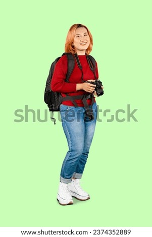 Young trendy photographer with red hair carrying camera backpack standing on isolated grey background
