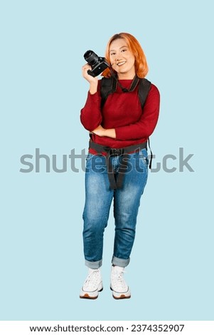 Young trendy photographer with red hair carrying camera backpack standing on isolated grey background