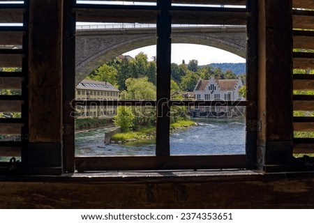 Looking through window of covered wooden bridge at the old town of Swiss City of Baden on a sunny summer day. Photo taken August 19th, 2023, Baden, Switzerland.