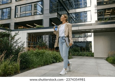 Stylish business woman drinking coffee during break time near office building and looks away Royalty-Free Stock Photo #2374354981