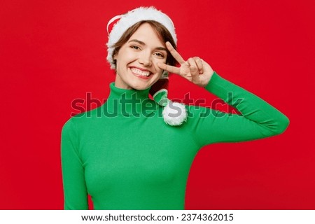Young smiling woman wear warm cozy green turtleneck Santa hat posing look camera cover eye with victory sign isolated on plain red background. Happy New Year 2024 celebration Christmas holiday concept