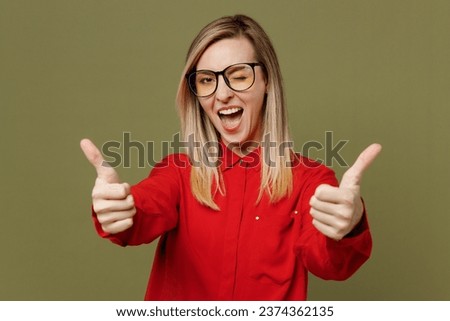 Young satisfied cheerful cool woman she wears red shirt casual clothes glasses showing thumb up like gesture wink blink eye isolated on plain pastel green background studio portrait. Lifestyle concept