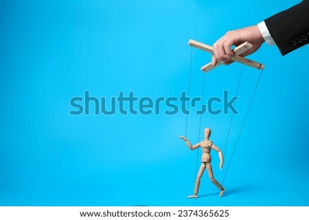 Man pulling strings of puppet on light blue background, closeup. Space for text Royalty-Free Stock Photo #2374365625