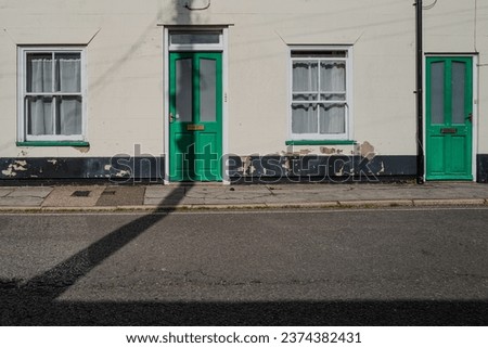 Abstract view of a pair of typical English terraced houses showing some sign of disrepair. A telegraph pole is casting a long shadow on a front door.
