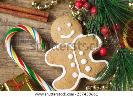 Homemade christmas painted gingerbread (gingerbread man and red present) on the wooden background with Christmas decorations, cones and candied orange. Selective focus on the man. Toned 