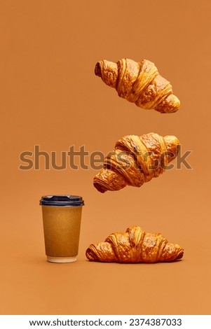 Levitating food. Crispy fresh croissants flying over coffee cup to go on brown background. Concept of food, bakery, breakfast ideas, taste, freshness. Poser. Copy space for ad Royalty-Free Stock Photo #2374387033