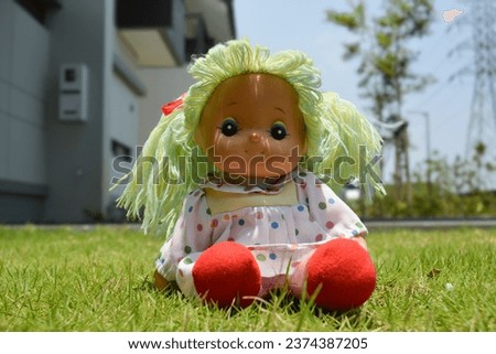 A Cute Doll With Green Hair Sitting On The Grass