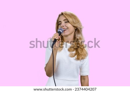 Pretty mature blond woman singing in microphone. Isolated on pink.