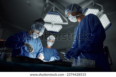 Teamwork, emergency and doctors or people in surgery procedure or healthcare operation in hospital. Night, low angle or surgeon in face mask or gloves help in dark operating room in medical clinic Royalty-Free Stock Photo #2374428515