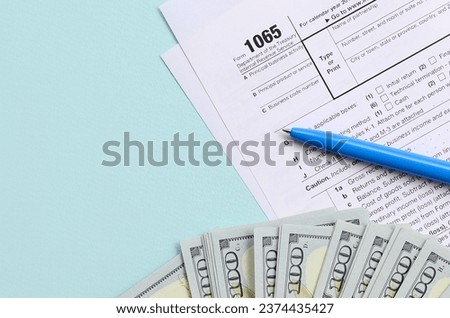 1065 tax form lies near hundred dollar bills and blue pen on a light blue background. US Return for parentship income. Royalty-Free Stock Photo #2374435427