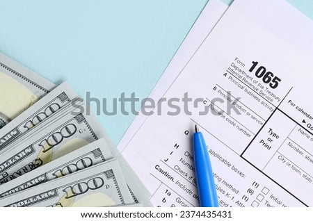 1065 tax form lies near hundred dollar bills and blue pen on a light blue background. US Return for parentship income. Royalty-Free Stock Photo #2374435431