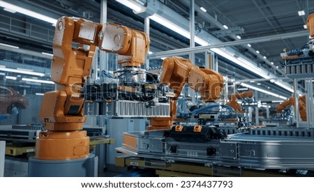 Advanced Orange Industrial Robot Arm Assemble EV Battery Pack on Automated Production Line. Modern Electric Car Smart Factory Equipped with Robotic Arms. Battery Module Installation Process. Royalty-Free Stock Photo #2374437793