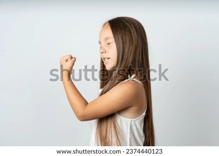 Portrait of funny beautiful kid girl wearing white dress shout yeah raise fists hands celebrate victory game competition